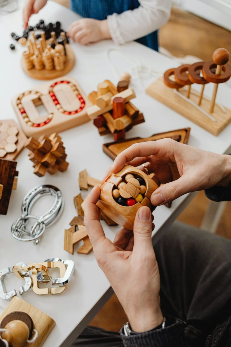 Close-up of hands holding a wooden puzzle among various wooden toys on a white table.